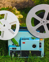 Vintage reel-to-reel tape recorder with two reels on a grassy background